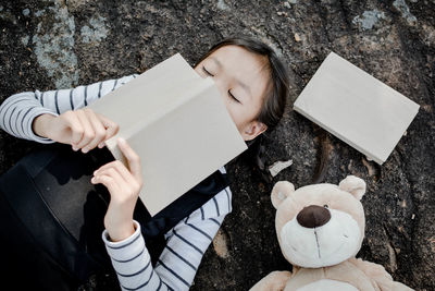 High angle view of girl with book lying by teddy bear at field