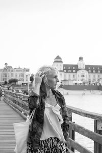 Woman standing by railing in city against clear sky