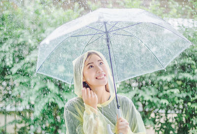 Smiling young woman holding umbrella during rainy season