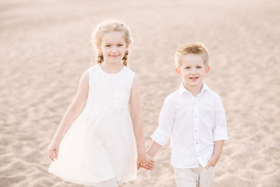 Portrait of smiling girl and boy holding hands at beach