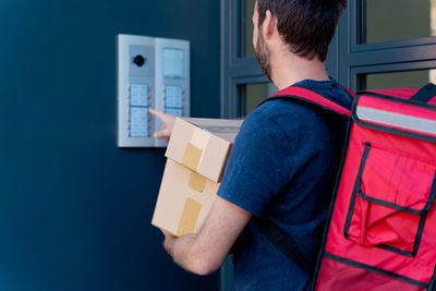 Midsection of delivery person holding parcel ringing doorbell
