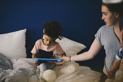 Mother carrying toddler giving digital tablet to son at home