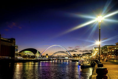 Illuminated bridge over river in city at night