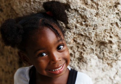 Close-up portrait of cute smiling girl against wall