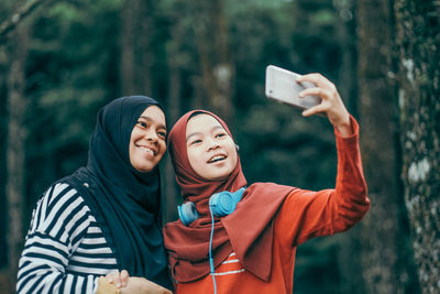 Smiling friends wearing hijab while taking selfie through mobile phone