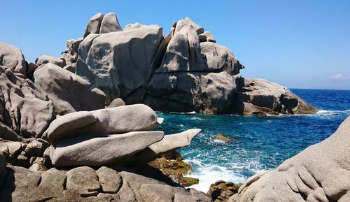 Rocks by sea against clear sky