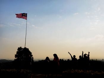 Silhouette people with malaysian flag against sky during sunset