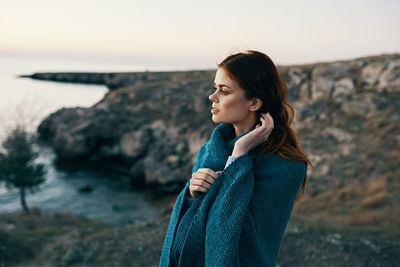 Young woman looking away while standing on rock