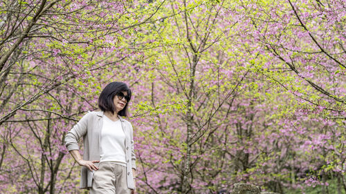 Woman standing by pink cherry blossom tree