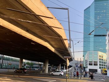 People on street by modern buildings against clear sky