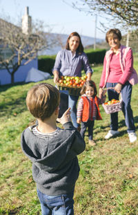 Rear view of boy photographing family from digital tablet on field