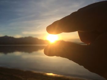 Close-up of silhouette hand against sea during sunset