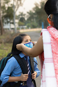 An indian school girl child going to school again after pandemic with her mother wearing nose mask