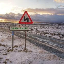 Road sign by sea against sky during sunset