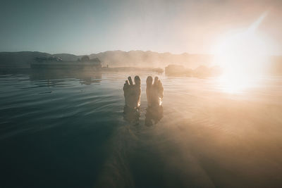 Low section of person relaxing in lake against sky during sunrise