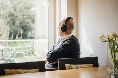 Senior man sitting at home, listening music, looking out of window