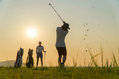 Rear view of people standing on field against sky during sunset