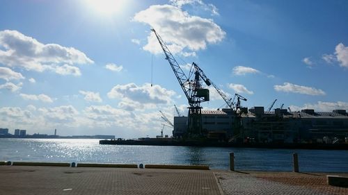 Cranes at commercial dock by sea against sky