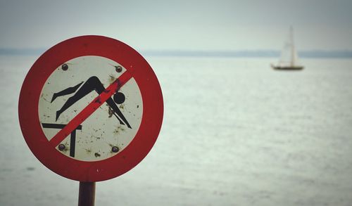 Close-up of warning sign on road by sea against sky