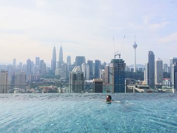 Side view of man swimming in pool against modern buildings in city