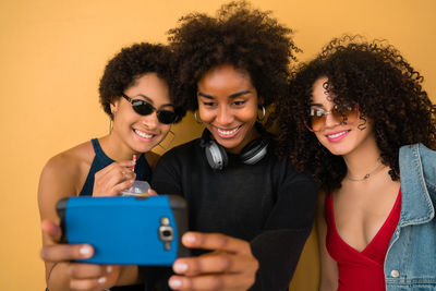 Smiling young woman taking selfie over smart phone with friends