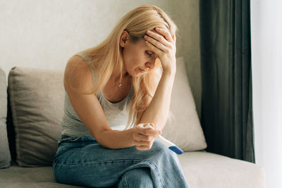 Upset sad woman holding pregnancy test while sitting on sofa at home.