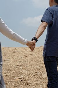 Midsection of couple holding hands while standing on field