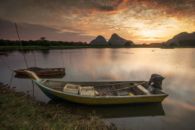 Boat moored on shore against sky during sunset