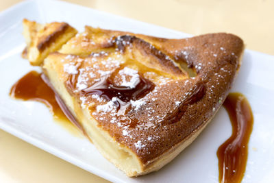 Close-up of fresh pie with syrup and powdered sugar served in plate on table