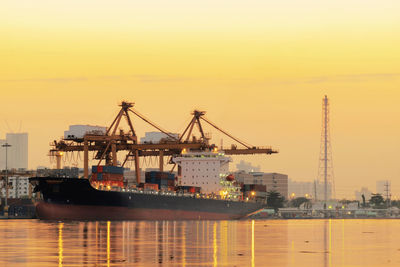 Cranes at commercial dock against sky during sunset