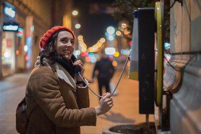 Young woman using phone while standing on street in city at night