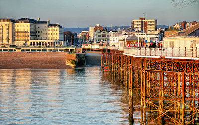 Bridge over river by buildings in city against sky