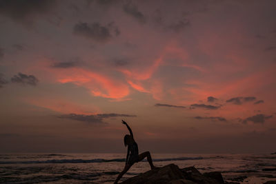 Silhouette woman exercising at beach against sky during sunset