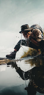 Reflection of man on water in lake against sky