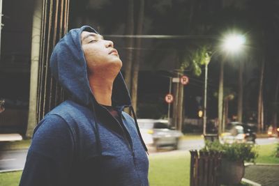 Man standing with eyes closed against trees at night