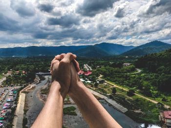 Cropped couple holding hands against cloudy sky