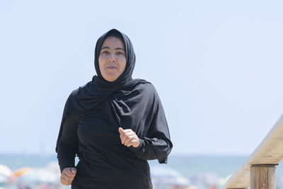 Portrait of young woman standing against clear sky