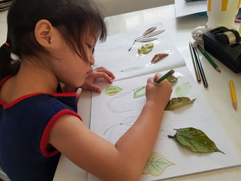 High angle view of girl drawing in book on table at home