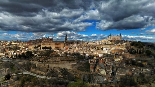 High angle view of alcazar of toledo in city against cloudy sky