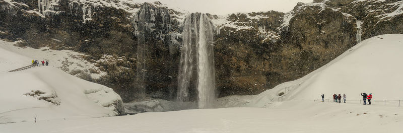 People on snow covered mountain against waterfall