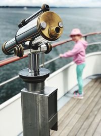 Close-up of hand-held telescope with girl standing on railing of boat in sea