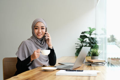 Portrait of young woman using mobile phone while sitting at home