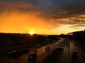 Cars on road against dramatic sky during sunset