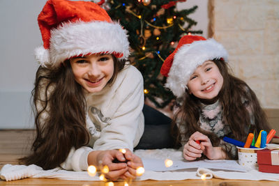 Portrait of smiling kids lying on floor against christmas tree