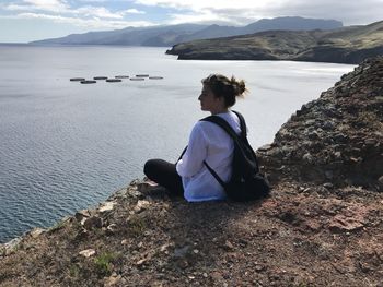 Rear view of woman sitting on rock by sea