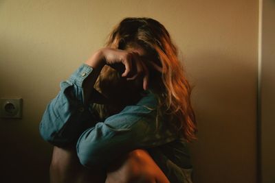 Sad woman sitting against wall at home