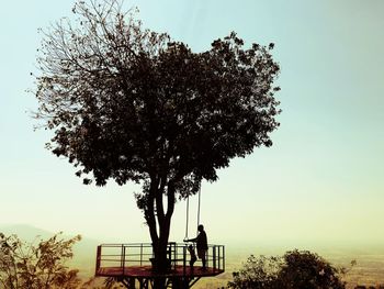 Silhouette tree by bench against clear sky