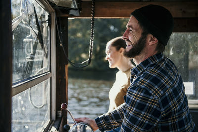 Cheerful man with woman standing in control room of boat