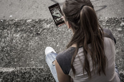 Rear view of teenage girl using phone on road