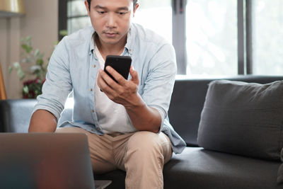 Young man using mobile phone while sitting on sofa